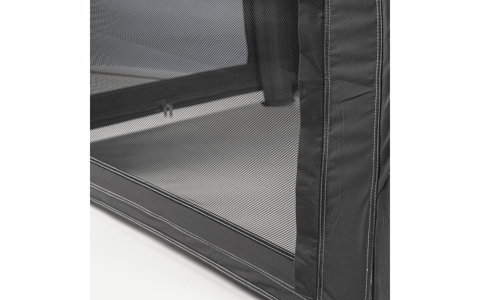 Close-up of black mesh with a fine weave, fabric edge with stitching on the right, horizontal bar visible behind the mesh, light surface underneath