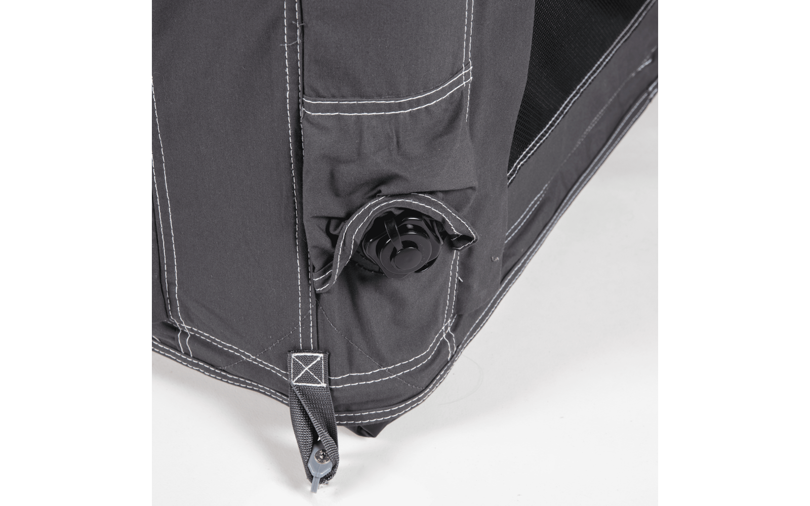Close-up of a dark gray fabric corner with white stitching, a black plastic round valve and a strap with metal eyelet