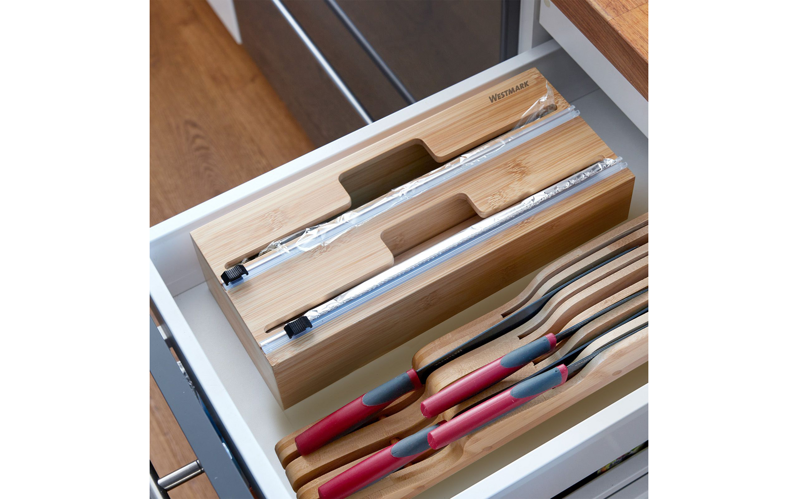 Cajón de cocina abierto con dos organizadores de bambú y varios cuchillos con mangos rojos