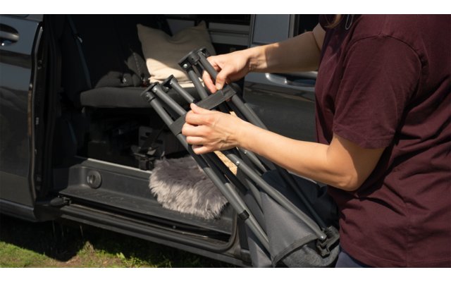 Person falten einen schwarzen Campingstuhl neben einem geöffneten Fahrzeug