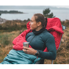 Femme assise en plein air sur l'herbe avec un sac à dos rouge tenant une tasse dans la main