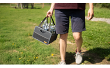 Personne portant une glacière sombre sur un chemin herbeux