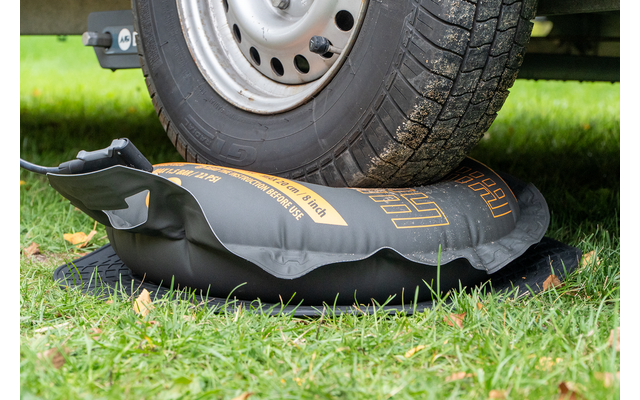 Fahrzeugreifen auf einer schwarzen aufblasbaren Tasche mit gelber Aufschrift, darunter eine schwarze Schutzmatte auf Gras