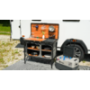 Buitenkookplaats met open kast voor een camper, draagbare stroomgenerator ernaast op de grond