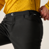 Close-up van taille en bovenbeen met zwarte broek en geel langarmshirt, rechterhand op de tailleband