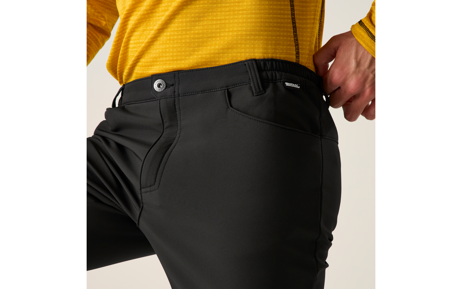Close-up van taille en bovenbeen met zwarte broek en geel langarmshirt, rechterhand op de tailleband