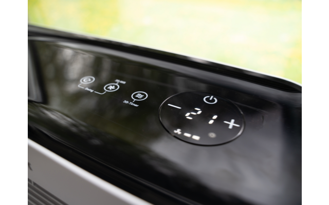 Schwarzes glänzendes Bedienfeld mit digitaler Anzeige "-21" und weißen Touch-Symbolen (Ein/Aus, +, -), verschwommener grüner Hintergrund