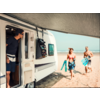 Wohnmobil mit geöffneter Tür auf einem Sandstrand; eine Person steht in der Tür und schaut hinaus; zwei Personen in Bademode laufen am Strand und tragen Schnorchelmasken und Flossen; Meer und Himmel im Hintergrund