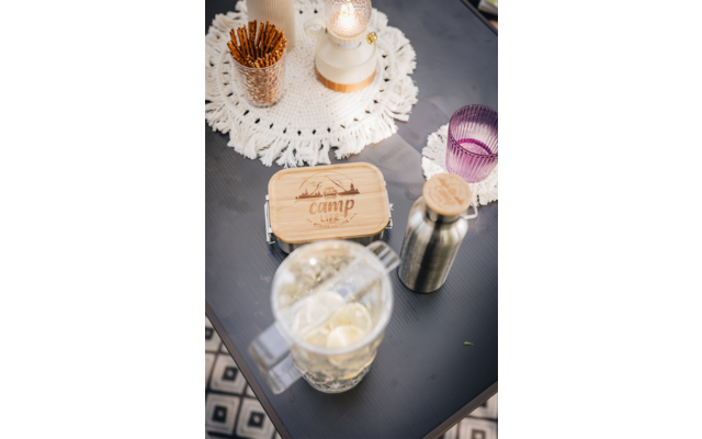 Holztablett mit Teelichtern und Kerze auf grauem Tisch, daneben ein Glas mit Eiswürfeln, ein Metallstrohhalm und ein lila Glas
