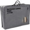 Grau rechteckige Tasche mit Griffen, Aufdruck 'OUTDOOR CARPET NAVA 2 X 3 M' und rundes Sichtfenster mit aufgerolltem gestreiftem Teppich