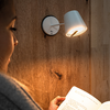 Seitliches Gesicht einer Person, weiße Wandlampe an Holzverkleidung, aufgeschlagenes Buch in den Händen, warmes Licht