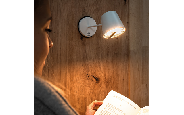Seitliches Gesicht einer Person, weiße Wandlampe an Holzverkleidung, aufgeschlagenes Buch in den Händen, warmes Licht