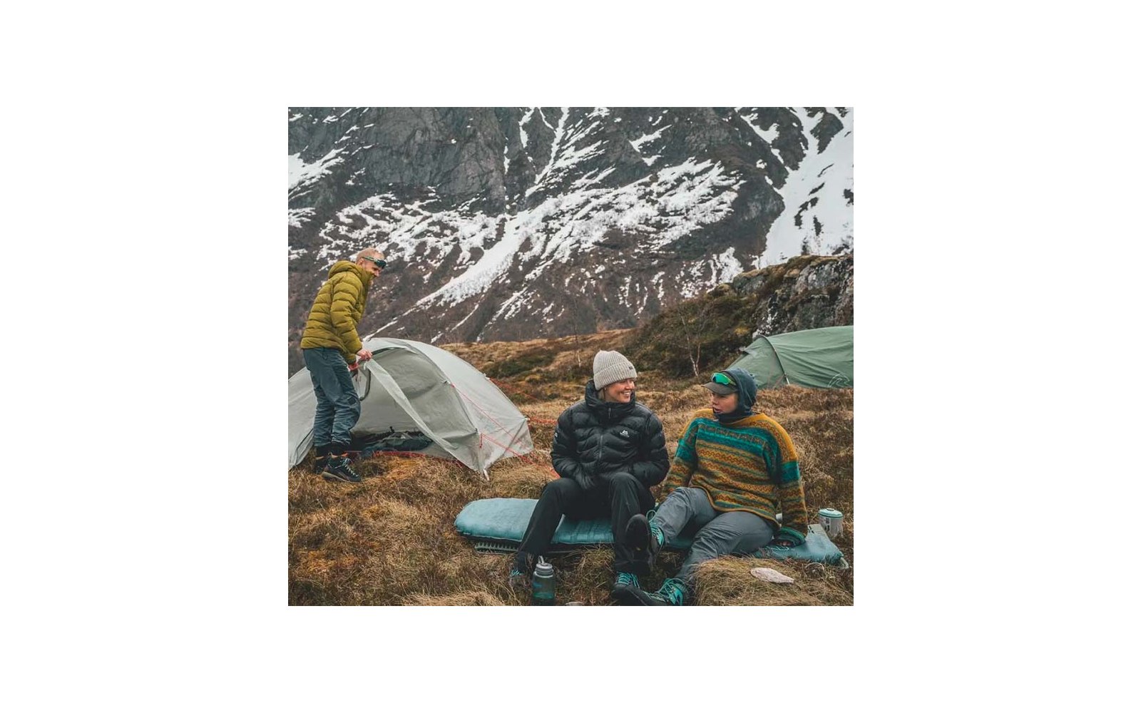 Drei Personen in Outdoor-Kleidung sitzen auf Felsen vor schneebedeckten Bergen
