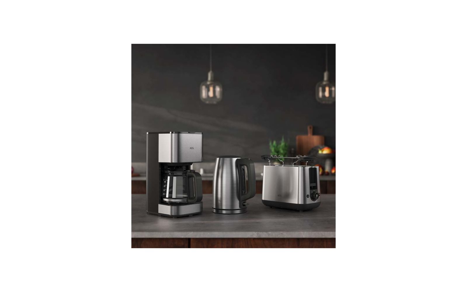 Cafetière avec verseuse en verre, bouilloire électrique et grille‑pain en acier inoxydable sur un plan de travail; deux suspensions et arrière‑plan de cuisine flou avec une plante et un panier de fruits