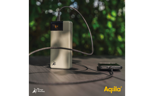 Een zilveren powerbank met een kabel op een houten tafel, een smartphone ernaast