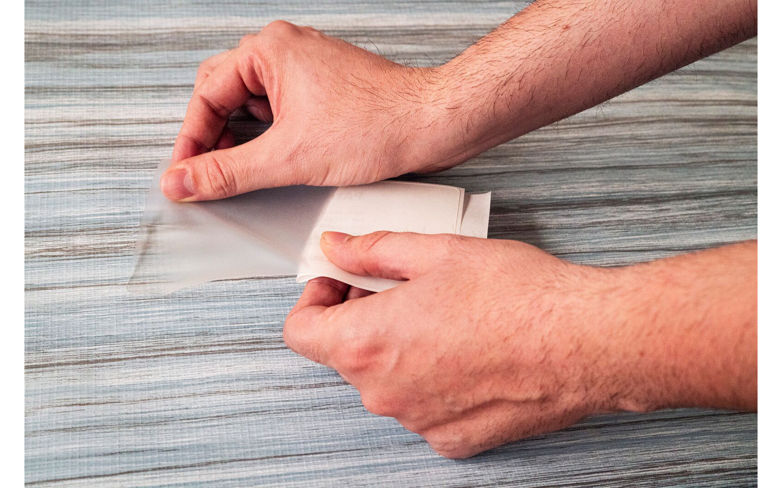 Deux mains glissent une carte blanche dans une pochette plastique transparente sur un tissu à rayures