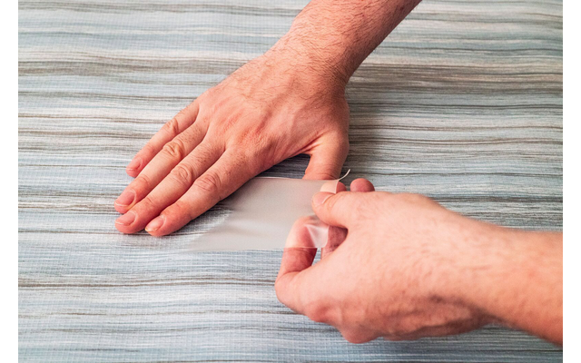 Deux mains pressant un morceau de ruban adhésif transparent sur un tissu à rayures bleu clair