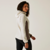 Femme aux cheveux bouclés portant une veste blanche, debout de côté