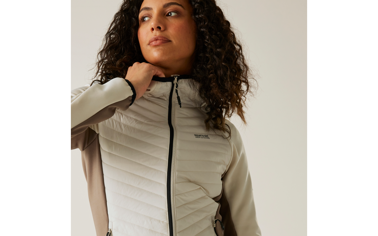 Femme aux cheveux bouclés portant une veste matelassée gris clair regardant vers le haut sur le côté