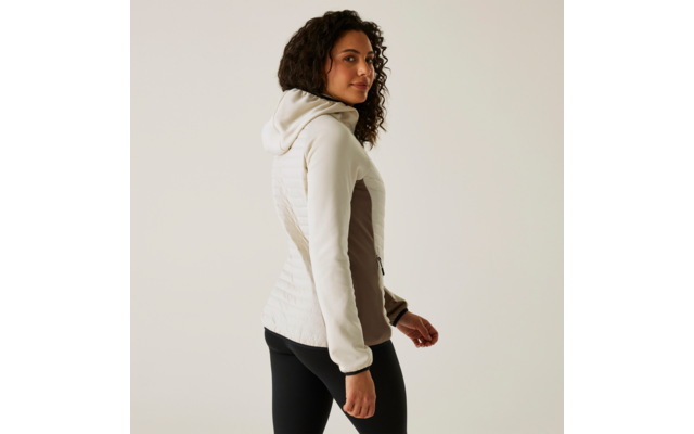 Femme aux cheveux bouclés portant une veste blanche, debout de côté