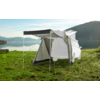 White camping tent with open entrance stands on a green meadow by a lake with mountains in the background