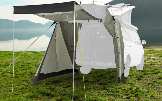 Weißes Campingzelt mit offenem Eingang steht auf einer grünen Wiese an einem See mit Bergen im Hintergrund