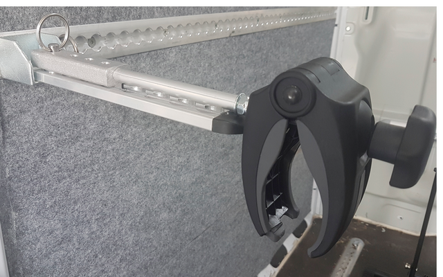 Gros plan d'une pince robotisée noire fixée à une tige métallique, avec un mur gris en arrière-plan
