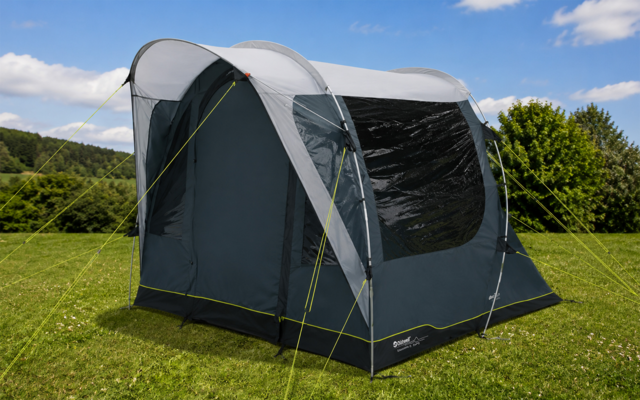 Donkergrijze vrijstaande tent met lichtgrijs dak, groot zijraam en gele scheerlijnen op groen gras; heuvels en blauwe lucht op de achtergrond