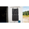 Ein weißes Wohnmobil mit einer an der Seite montierten schwarzen Solaranlage, im Hintergrund Bäume und eine Wiese