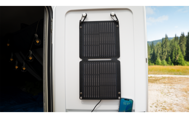 Ein weißes Wohnmobil mit einer an der Seite montierten schwarzen Solaranlage, im Hintergrund Bäume und eine Wiese