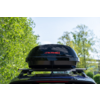 Box da tetto nero con scritta rossa KRAMER montato su portapacchi auto, alberi e cielo sullo sfondo