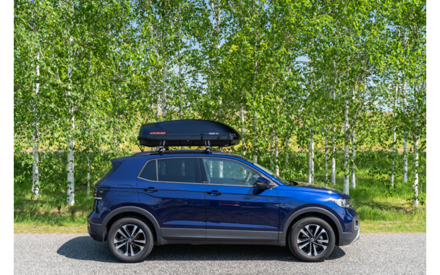 SUV blu con box da tetto su una strada davanti a una fila di betulle
