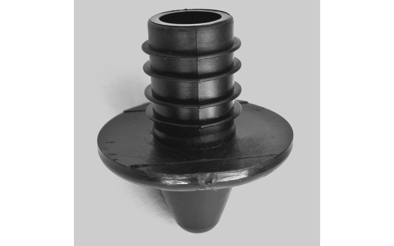 Pièce en plastique noire avec bride ronde, tige cylindrique nervurée et pointe conique, sur fond clair