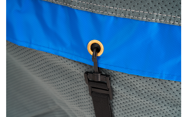 Close-up of a blue fabric band with a gold metal grommet, a black cord threaded through the grommet, a black plastic buckle on a black strap, and gray mesh fabric in the background