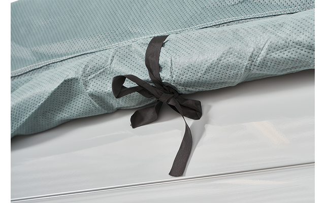 Close-up of a light green fabric with a fine dotted pattern and a black fabric bow on a white surface