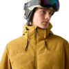 Person mit Skihelm und hochgeschobener Skibrille, gelbe Jacke mit hohem Kragen, Blick nach rechts, heller einfarbiger Hintergrund