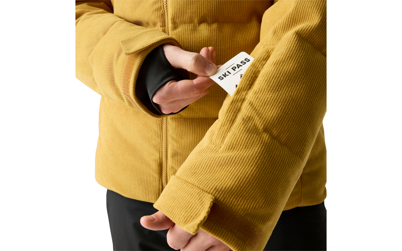 Hände ziehen eine weiße Karte mit schwarzem Text 'SKI PASS' aus der Ärmeltasche einer senfgelben Cordjacke; schwarzer Innenärmel sichtbar