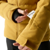 Hände ziehen eine weiße Karte mit schwarzem Text 'SKI PASS' aus der Ärmeltasche einer senfgelben Cordjacke; schwarzer Innenärmel sichtbar