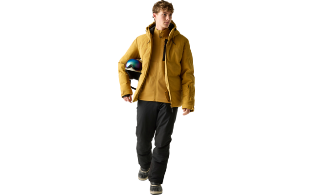 Person in gelber gesteppter Jacke hält Helm mit schillerndem Visier unter dem Arm, trägt schwarze Hose und Stiefel, geht vor hellem einfarbigem Hintergrund
