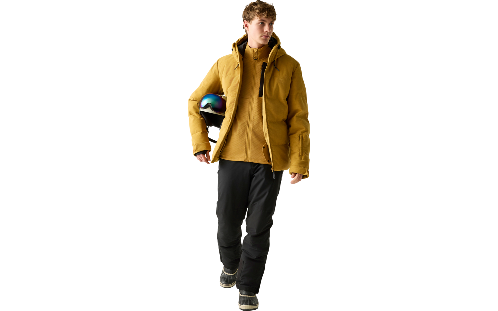 Person in gelber gesteppter Jacke hält Helm mit schillerndem Visier unter dem Arm, trägt schwarze Hose und Stiefel, geht vor hellem einfarbigem Hintergrund