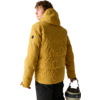 Person von hinten/seitlich, trägt senfgelbe gesteppte Kapuzenjacke, hält einen beigen und schwarzen Helm in einer Hand, heller einfarbiger Hintergrund
