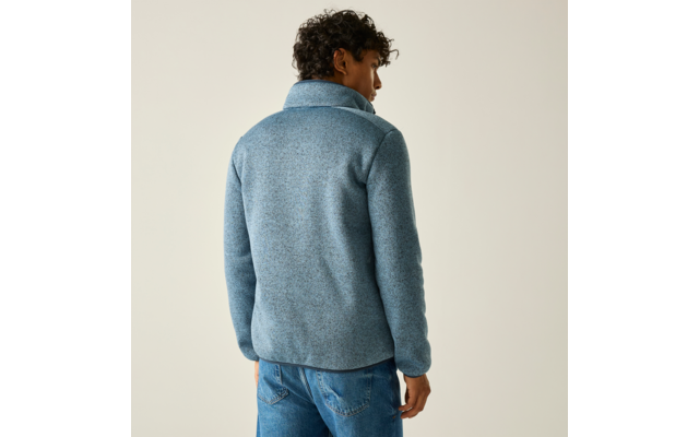 Person seen from behind wearing a light blue fleece jacket with a high collar and blue jeans against a plain light background