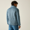 Person seen from behind wearing a light blue fleece jacket with a high collar and blue jeans against a plain light background