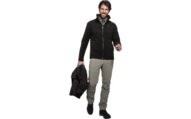 Persoon op witte achtergrond met zwarte fleece met ritssluiting, geruit overhemd, kaki broek en zwarte schoenen; houdt een zwarte jas in de linkerhand