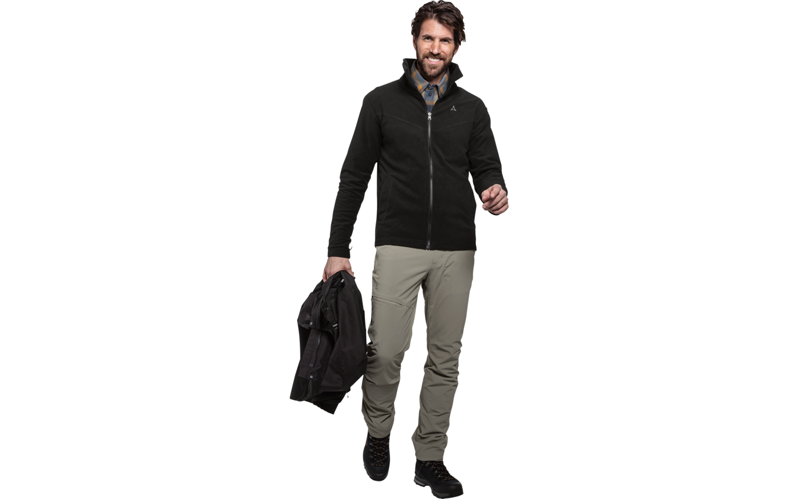 Persoon op witte achtergrond met zwarte fleece met ritssluiting, geruit overhemd, kaki broek en zwarte schoenen; houdt een zwarte jas in de linkerhand