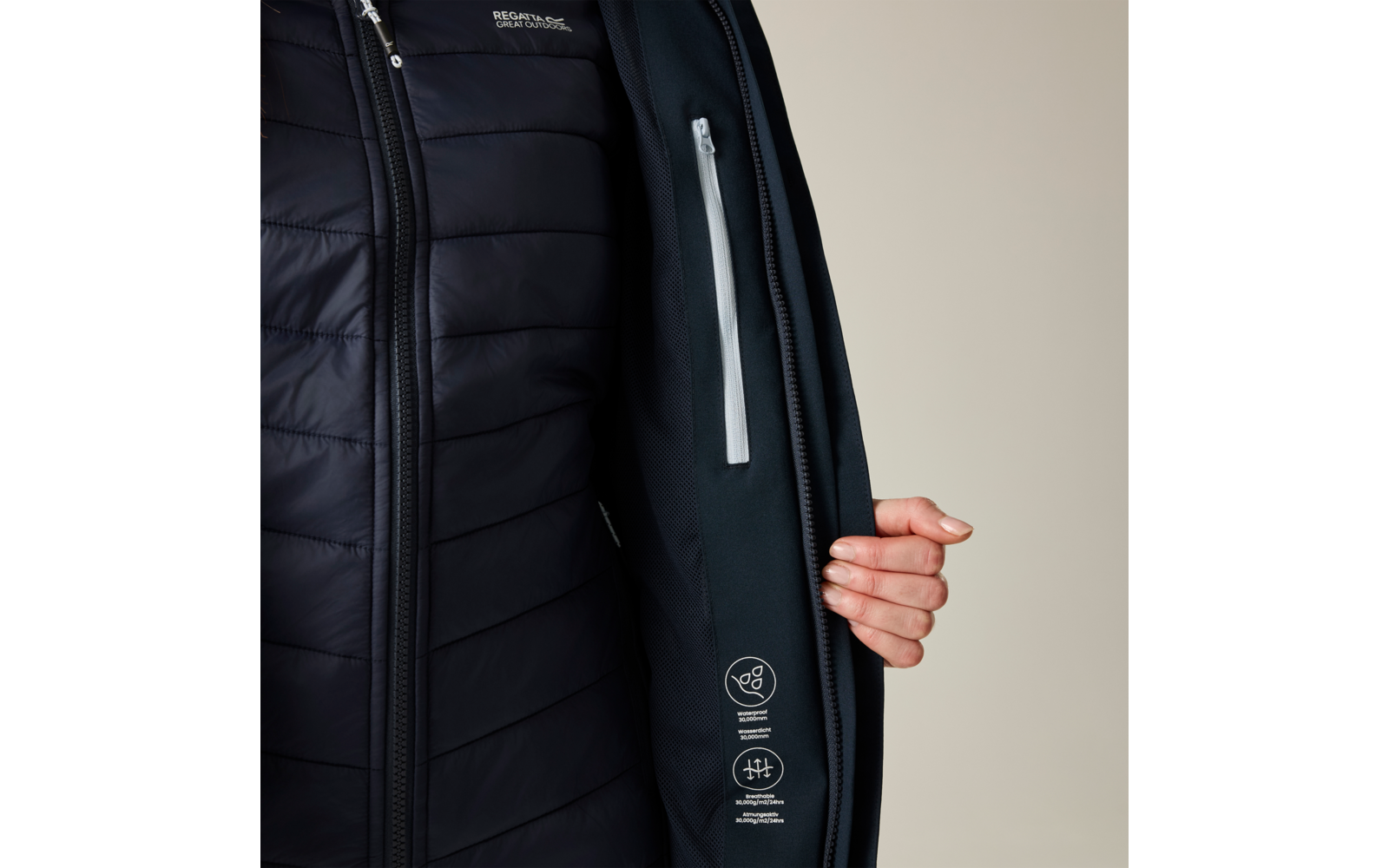 Geöffnete dunkelblaue gesteppte Jacke, Innenseite mit weißem Reißverschlussfach, Hand hält die Jacke offen, weiße Piktogramme innen