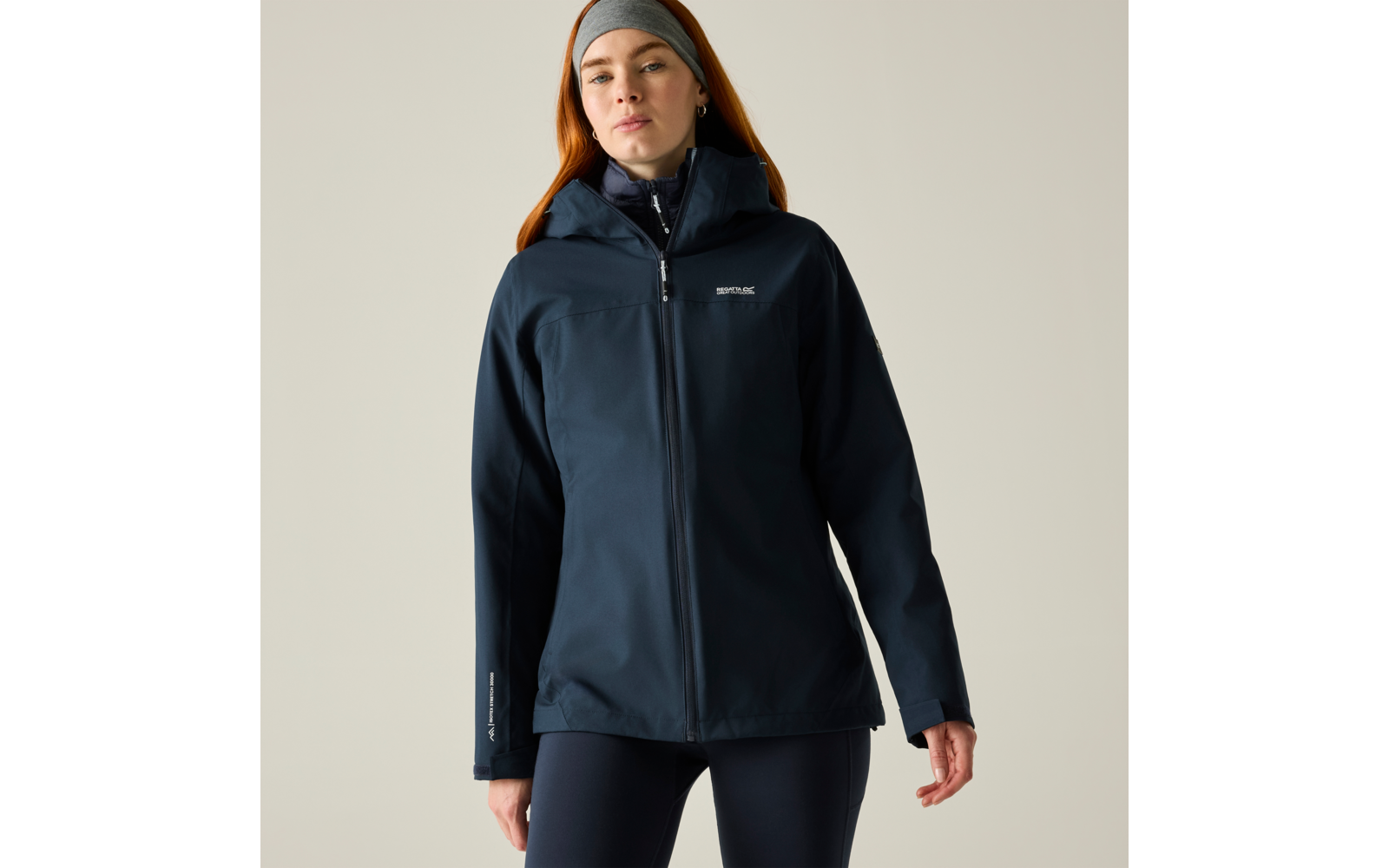 Person in dunkelblauer Jacke mit Reißverschluss und grauem Stirnband, frontal stehend, Hände seitlich, heller Hintergrund