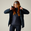 Person mit langem roten Haar und Stirnband zieht Außenjacke über Steppjacke an, Augen geschlossen, heller Hintergrund