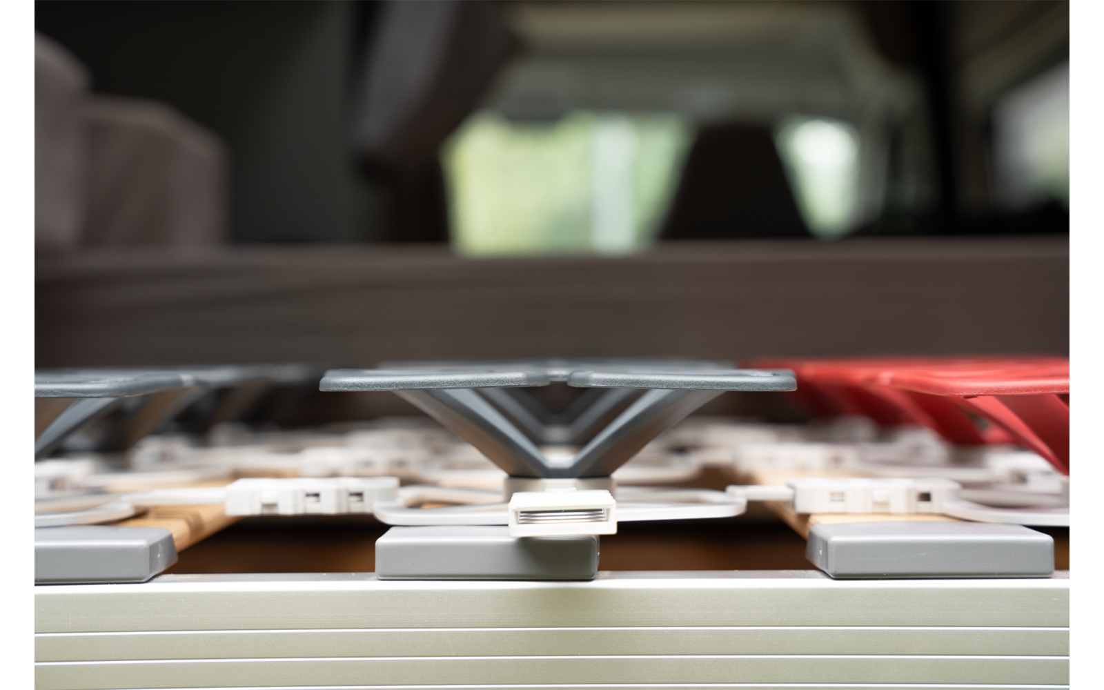 Close-up van meerdere kunststofsteunen met komvormige bovenkanten op een metalen rand; grijs, beige en rood; onscherpe achtergrond met raamlicht