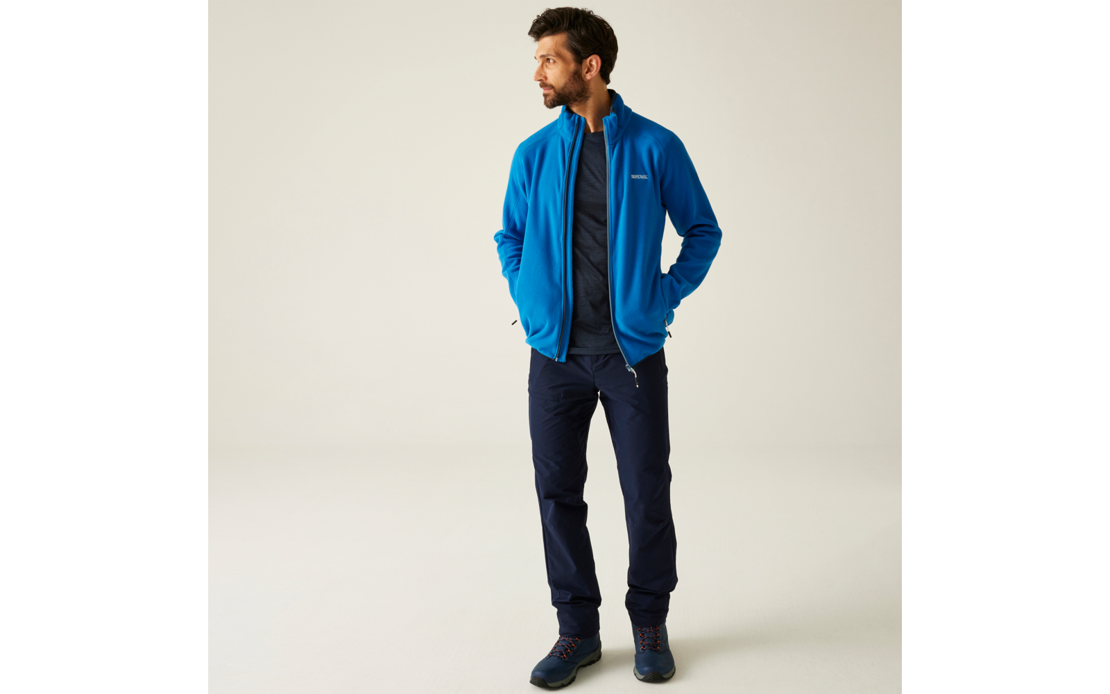 Mann mit blauer Jacke und dunkler Hose steht vor hellem Hintergrund